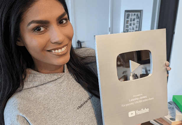 Woman smiling holding YouTube Silver Play Button award for 100,000 subscribers.